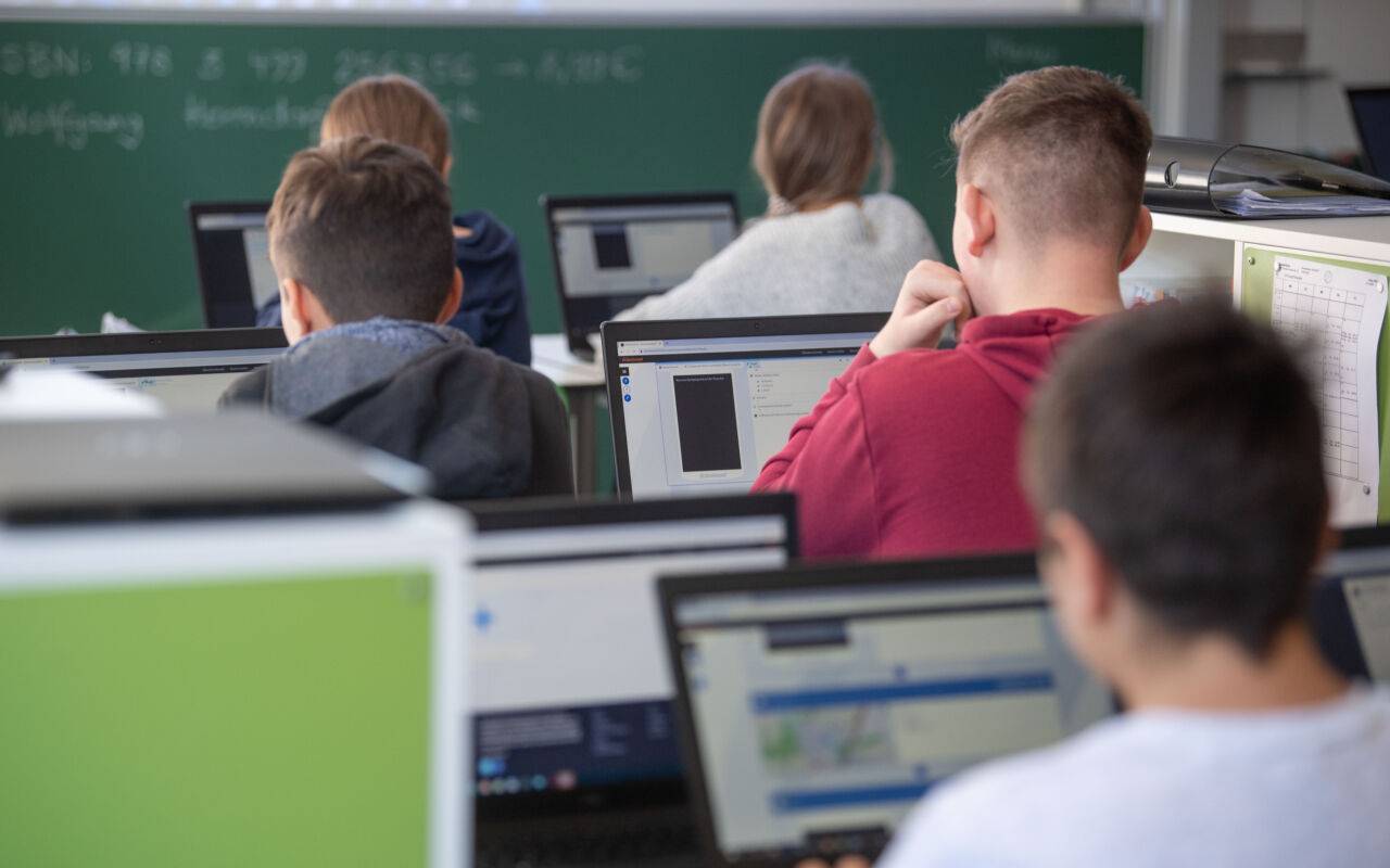 Beschreibung  Schülerinnen und Schüler nehmen im Klassenzimmer einer 9. Klasse der Gemeinschaftsschule Leutenbach am Geografieunterricht mit Hilfe von Laptops und Tablets teil.
