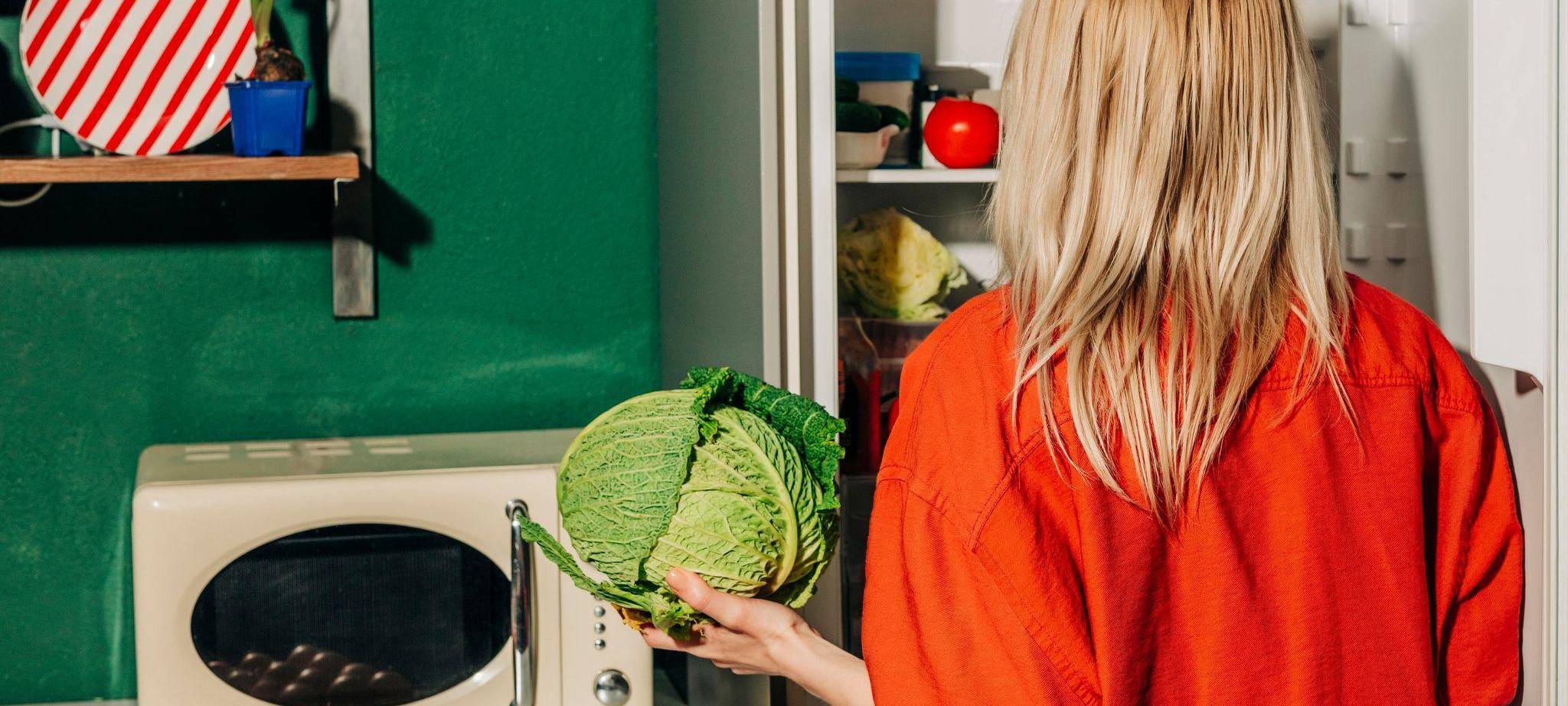 Eine Frau hält einen Kohl vor einem offenen Kühlschrank