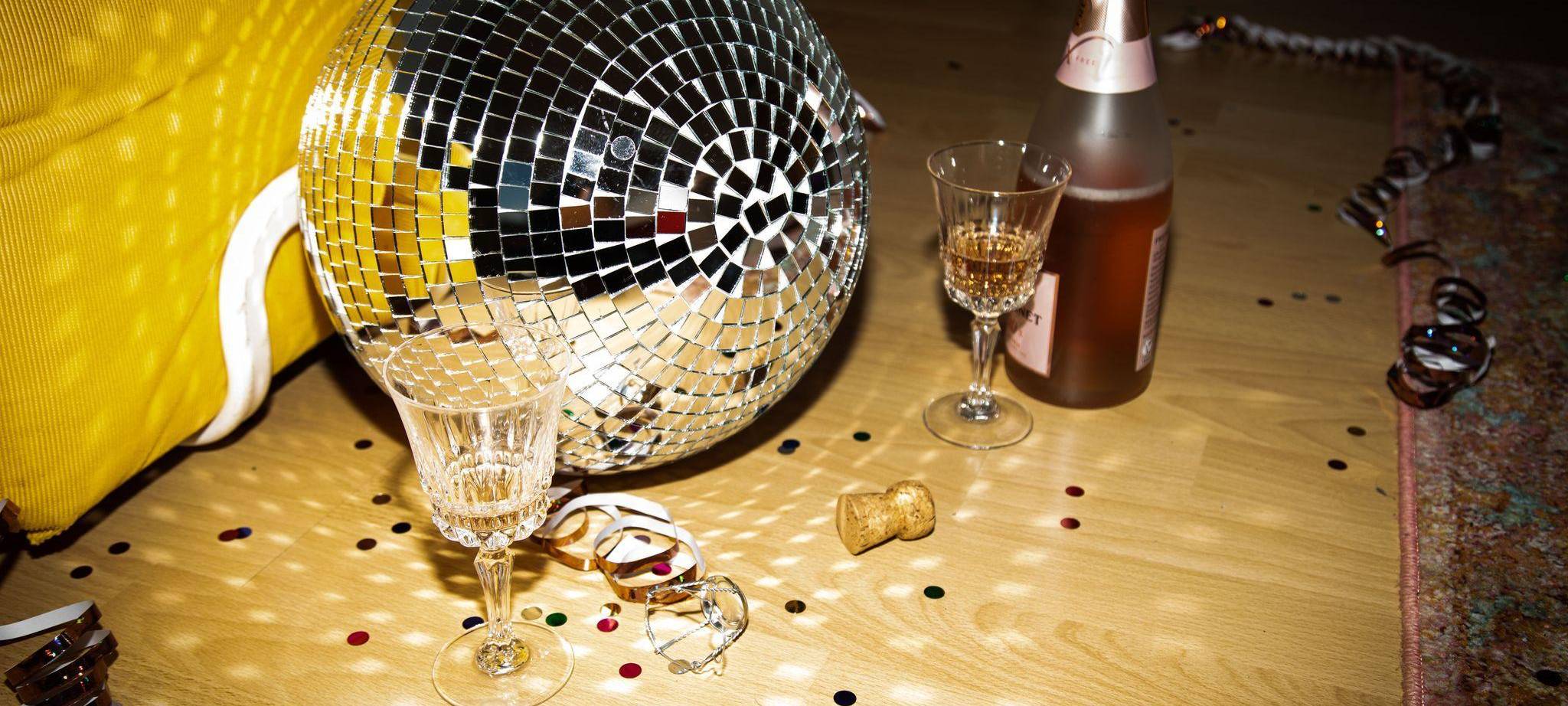 Discokugel liegt neben Sektflaschen und Gläsern auf dem Boden