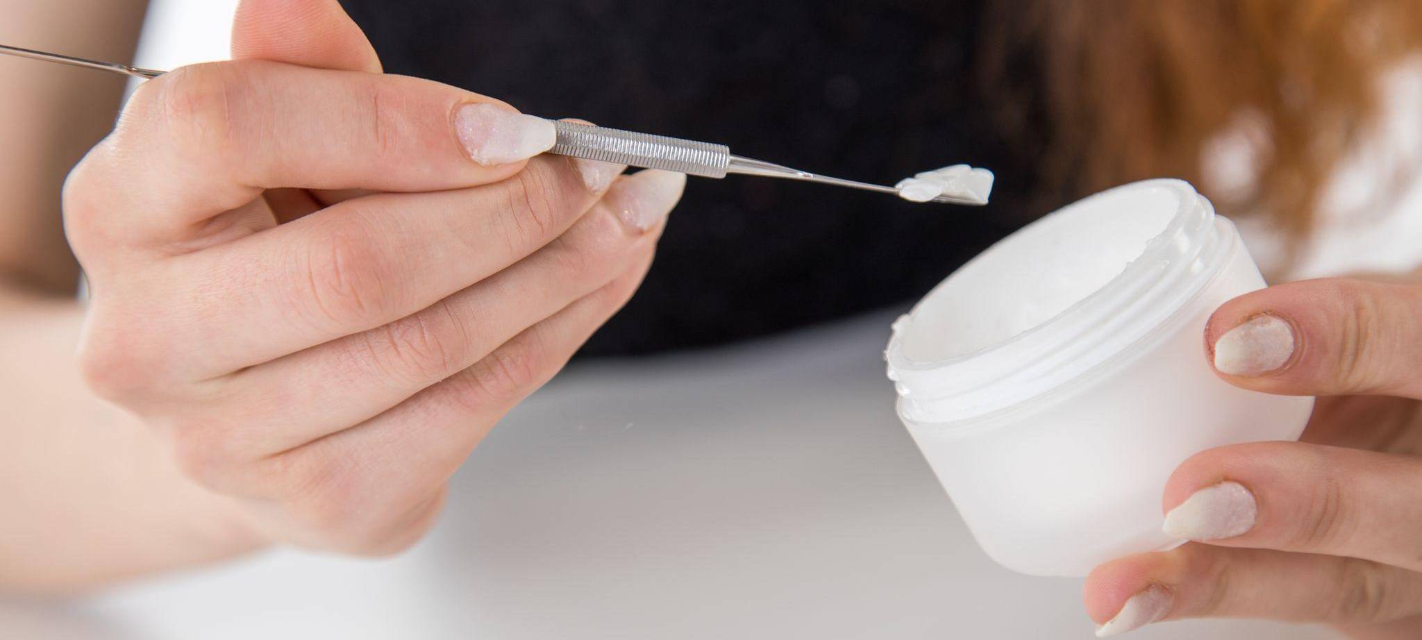 Eine Frau entnimmt mit einem Spatel Creme aus einem Tiegel