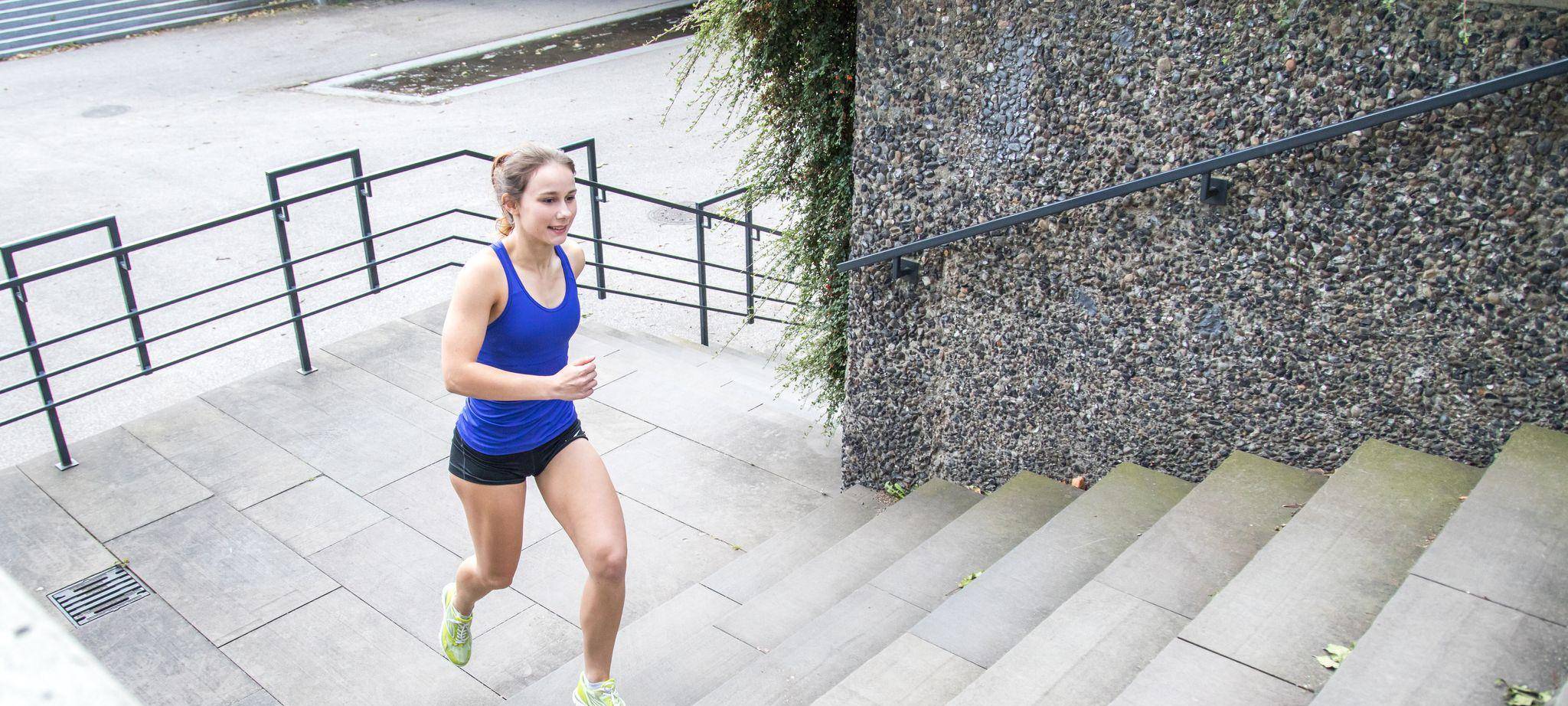 Frau joggt im Park die Stufen einer Treppe empor