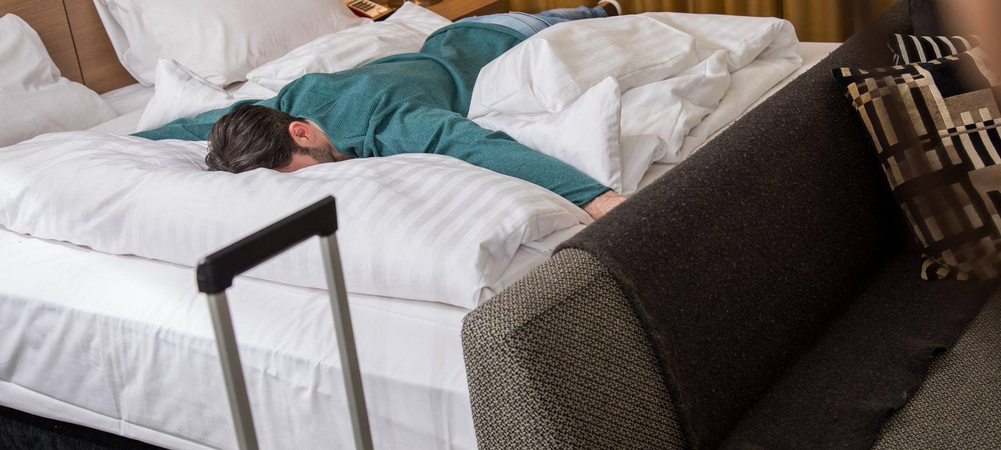 Ein Mann liegt erschöpft auf einem Bett in einem Hotelzimmer